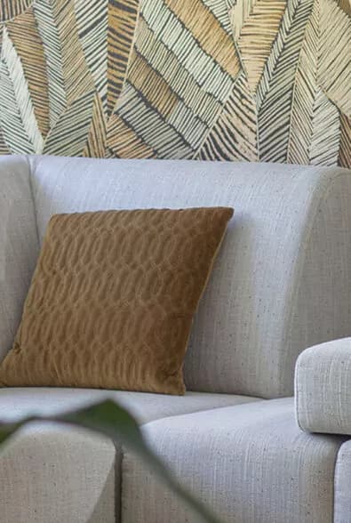 Lichte bank met kussen voor een behang met bladerenprint in de showroom Heemskerk